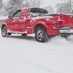 image of red pickup truck 4x4 spinning wheels snowy icy street